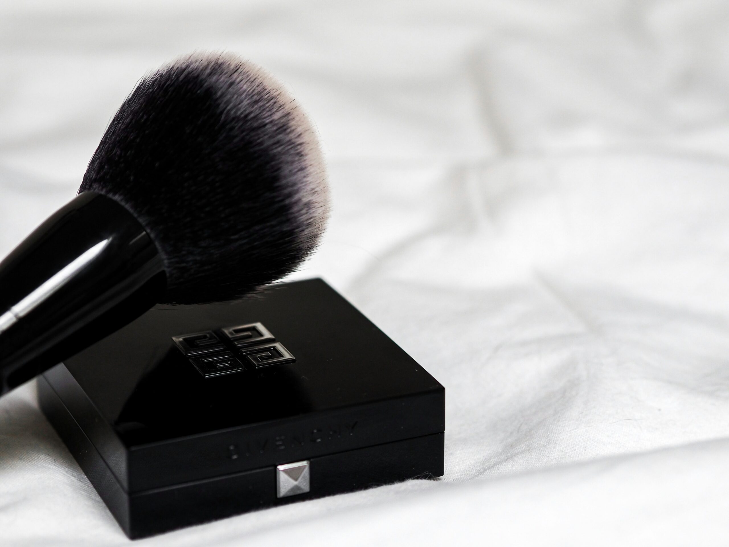Black makeup brush resting on a black compact case against a dark background.